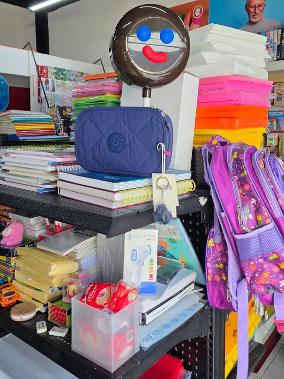 Libretas y cuadernos apilados, hojas de colores y mochilas moradas colgadas al lado