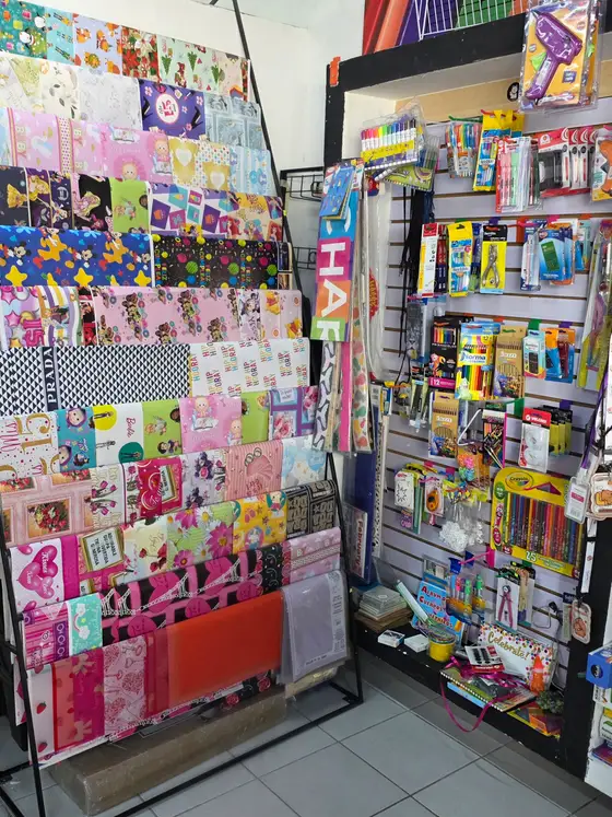 Exhibidor de pliegos de papel de regalo, y junto a él la pared de útiles escolares