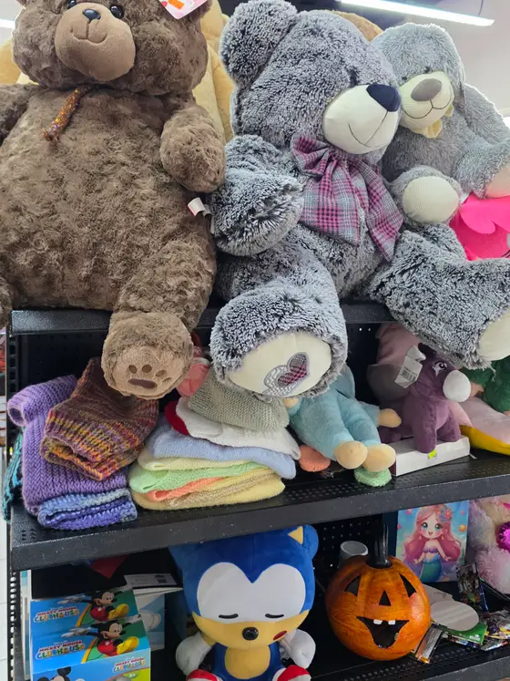 Peluches grandes de oso en el estante alto, y debajo ropa tejida de bebé