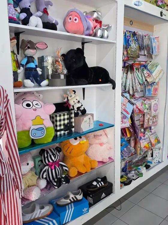 Librero blanco lleno de peluches, con globos y artículos de fiesta en la pared de al lado
