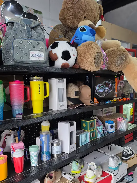 Estante de termos y vasos de colores, con gorras, peluches y mochilas alrededor